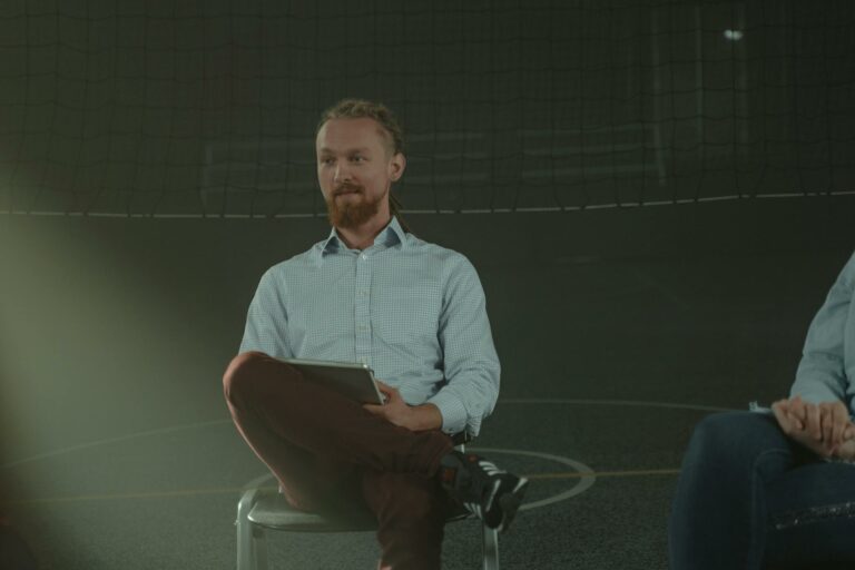 A man holds a meeting in a dimly lit room, engaging with others in a discussion.