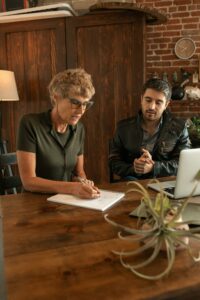 An adult woman and man collaborating over educational material at a wooden table indoors.