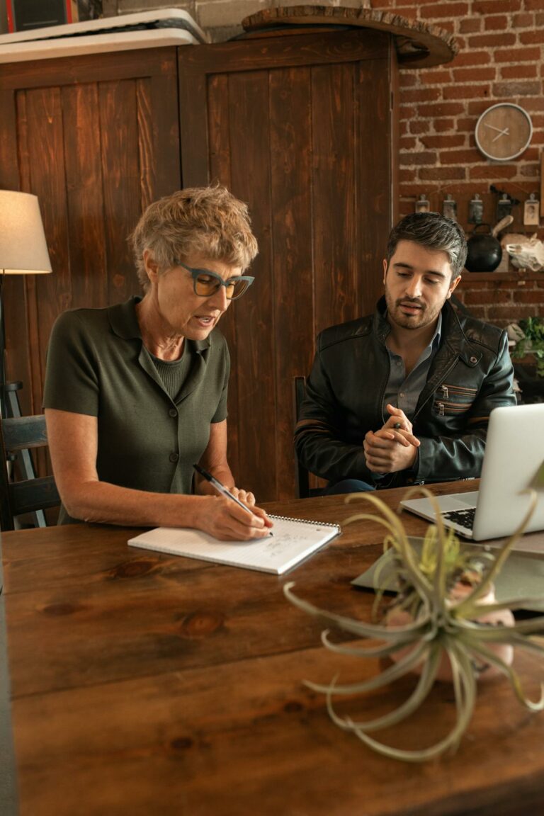 An adult woman and man collaborating over educational material at a wooden table indoors.